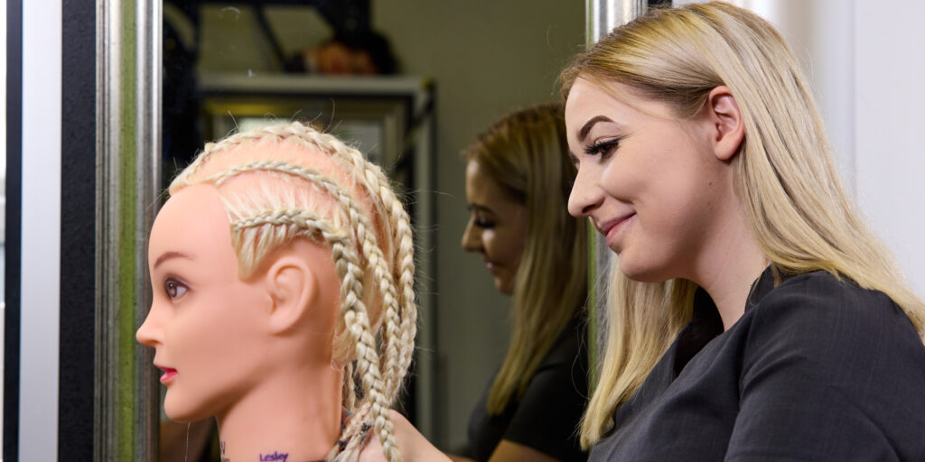 Photo of a student styling the hair of a hairdressing mannequin
